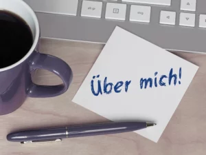 Arbeitsplatz mit Kaffeetasse, Kugelschreiber, Post-It mit Schriftzug "Über mich!"