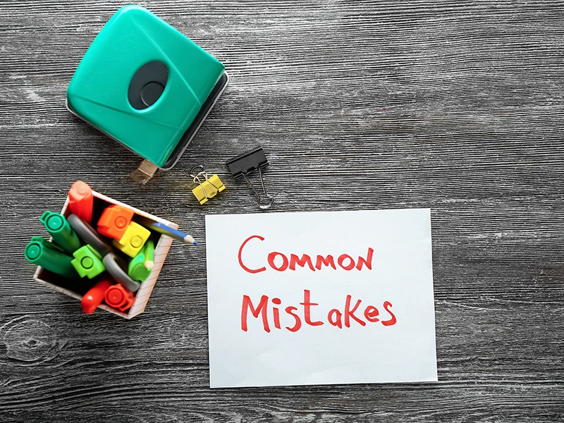Holzfläche im Hintergrund, Locher, Box mit Stiften und Post-It mit Aufschrift "common mistakes"