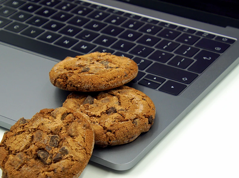 3 Cookies liegen auf der Tastatur eines aufgeklappten Laptos.